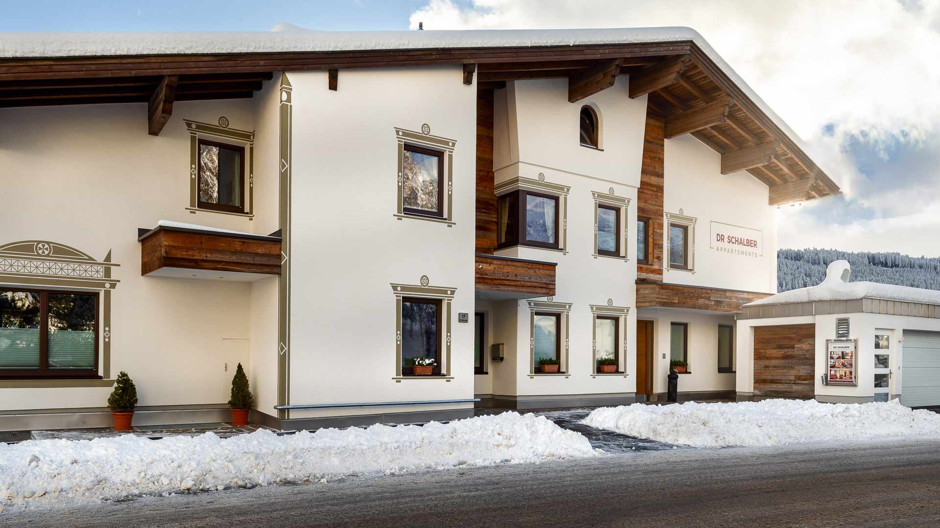 Alpenhaus „Dr. Schalber Appartements“ im Winter mit verschneitem Dach und Bergkulisse im Hintergrund.