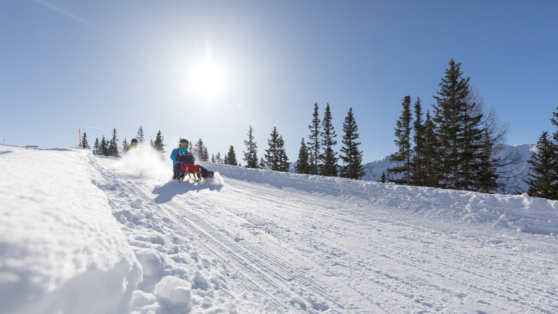 Familienrodelspaß auf verschneiter Piste bei strahlendem Sonnenschein in der Winterwelt von Serfaus-Fiss-Ladis.