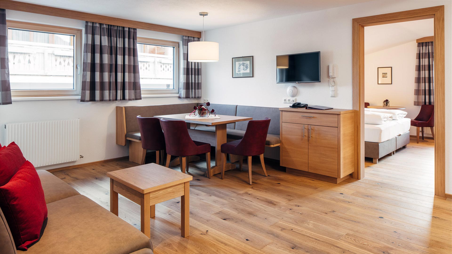Gemütliche Ferienwohnung mit modernem Holzinterieur, Essecke, Sofa und direktem Blick ins helle Schlafzimmer.